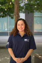 The image is Denise standing in front of a tree in the Social Justice Plaza